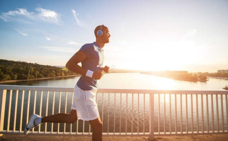 A young man running on the bridge along a river. Lens flare, warm tones.